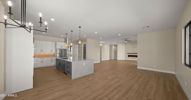 kitchen with a kitchen island with sink, white cabinets, pendant lighting, light hardwood / wood-style flooring, and stainless steel refrigerator with ice dispenser