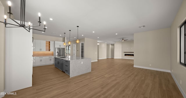 kitchen featuring a kitchen island with sink, ceiling fan with notable chandelier, decorative light fixtures, hardwood / wood-style flooring, and white cabinetry