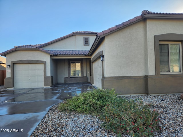 view of front of house featuring a tiled roof, concrete driveway, an attached garage, and stucco siding