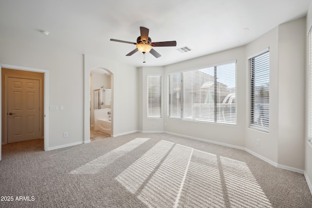 unfurnished bedroom with arched walkways, ensuite bathroom, light colored carpet, visible vents, and baseboards