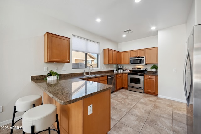 kitchen featuring a peninsula, a sink, visible vents, a kitchen breakfast bar, and appliances with stainless steel finishes