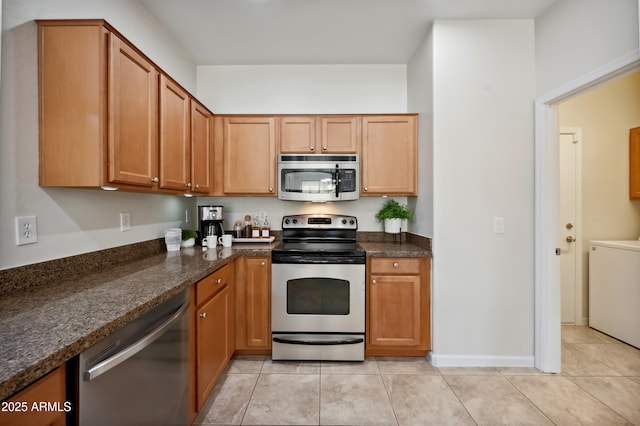 kitchen with washer / dryer, baseboards, dark stone counters, stainless steel appliances, and light tile patterned flooring