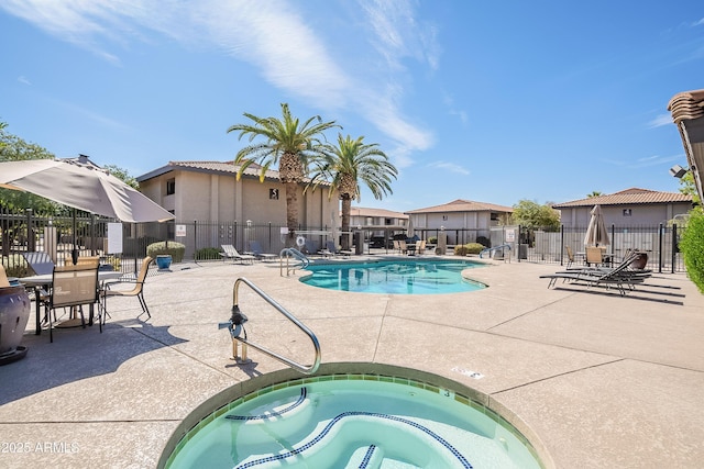 community pool with a patio area, a hot tub, and fence