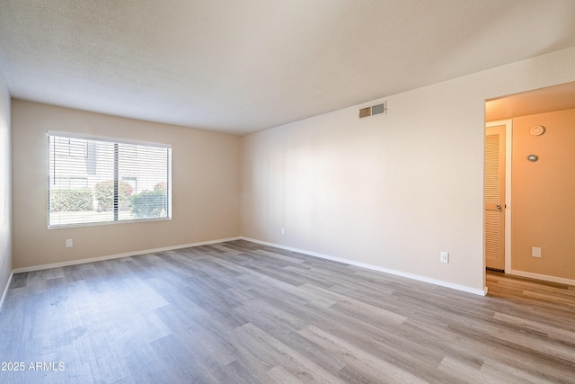 unfurnished room featuring light wood-style flooring, visible vents, and baseboards