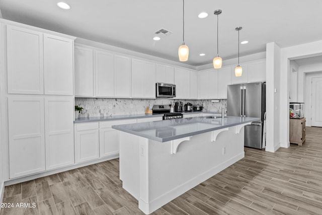 kitchen featuring appliances with stainless steel finishes, a kitchen island with sink, pendant lighting, light hardwood / wood-style flooring, and white cabinets