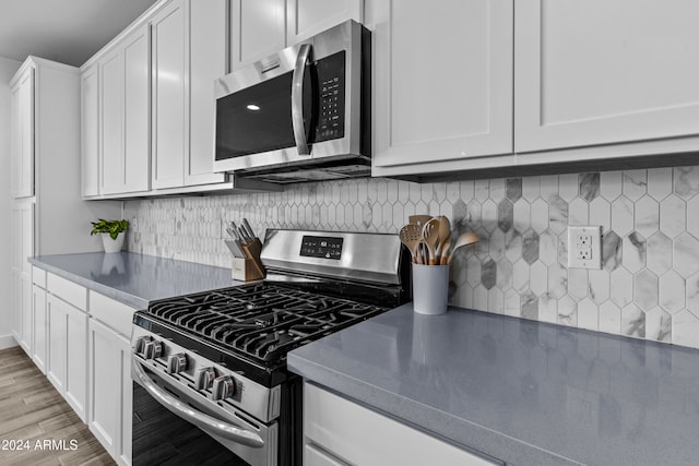 kitchen featuring decorative backsplash, light wood-type flooring, stainless steel appliances, and white cabinetry