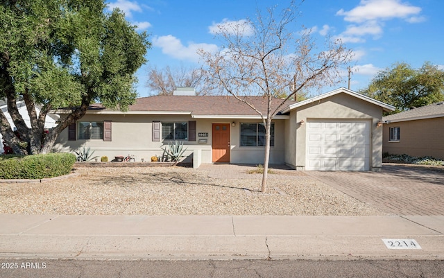 ranch-style house with stucco siding, an attached garage, a chimney, and decorative driveway