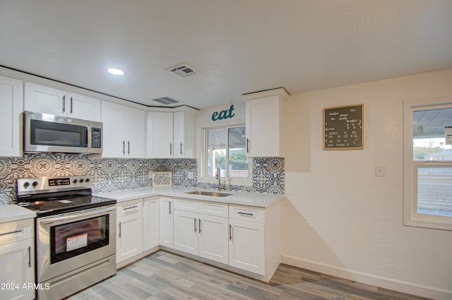 kitchen with sink, white cabinetry, stainless steel appliances, decorative backsplash, and light wood-type flooring