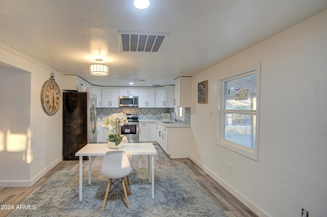 kitchen with sink, stainless steel appliances, tasteful backsplash, wood-type flooring, and white cabinets