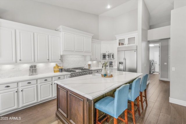 kitchen with white cabinets, a center island, a towering ceiling, stainless steel appliances, and independent washer and dryer