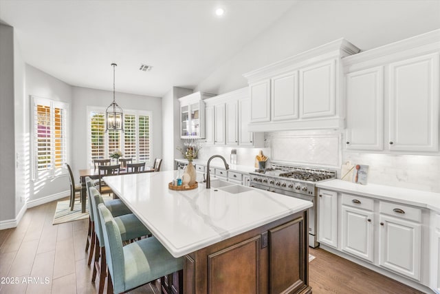 kitchen with tasteful backsplash, a center island with sink, sink, stainless steel range, and white cabinets