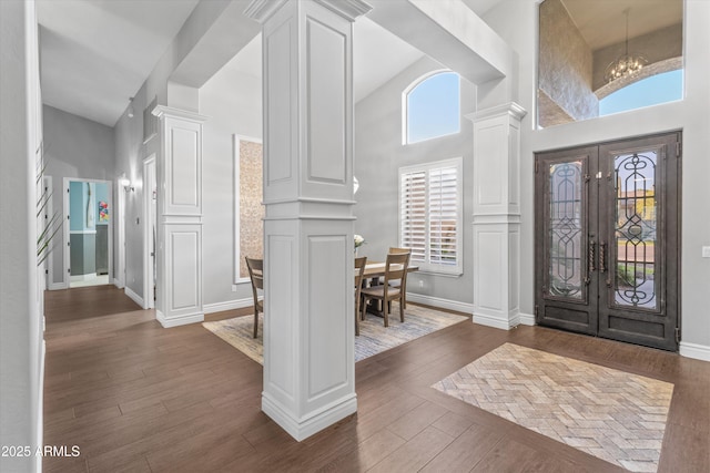 foyer entrance featuring a notable chandelier, a towering ceiling, french doors, dark hardwood / wood-style flooring, and ornate columns