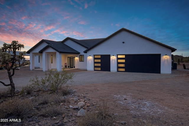 view of front facade featuring a garage, dirt driveway, a tile roof, central air condition unit, and stucco siding