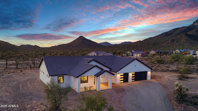 view of front of home with a tile roof, dirt driveway, a mountain view, and stucco siding