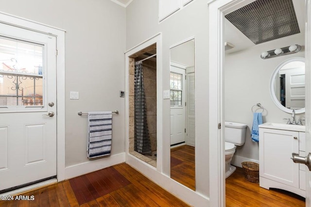 bathroom with baseboards, toilet, vanity, wood-type flooring, and tiled shower