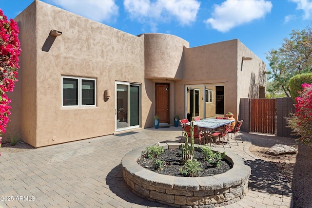 rear view of house with outdoor dining space, a patio, fence, and stucco siding