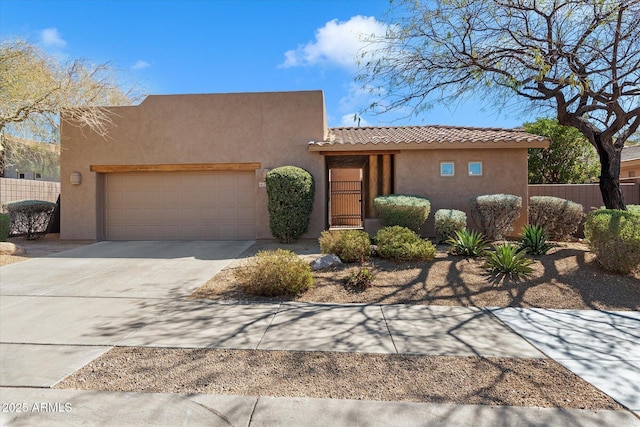 pueblo revival-style home featuring a garage, fence, and stucco siding