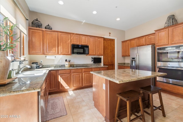 kitchen with a breakfast bar, a kitchen island, a sink, light stone countertops, and black appliances