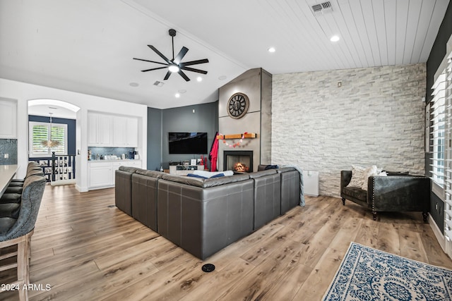 living room with ceiling fan, a stone fireplace, light hardwood / wood-style flooring, vaulted ceiling, and wood ceiling