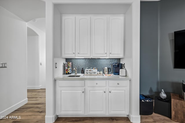 bar featuring hardwood / wood-style flooring, decorative backsplash, white cabinetry, and sink