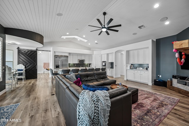 living room featuring a barn door, light hardwood / wood-style floors, ceiling fan, and wooden ceiling