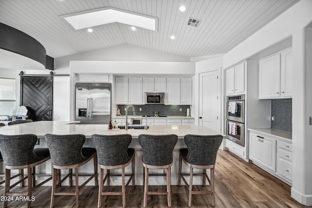 kitchen featuring vaulted ceiling with skylight, a barn door, tasteful backsplash, white cabinetry, and stainless steel appliances