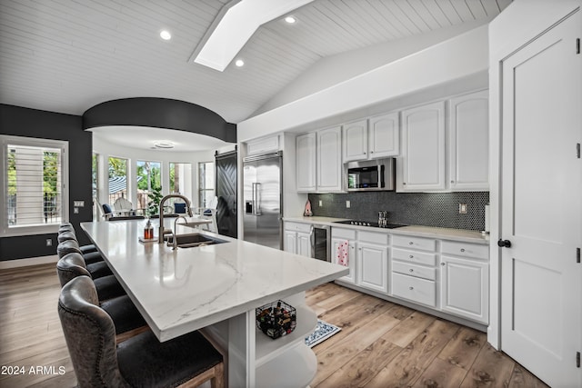 kitchen with a kitchen bar, appliances with stainless steel finishes, sink, white cabinetry, and an island with sink