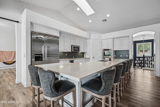 kitchen with white cabinets, backsplash, vaulted ceiling, and a spacious island