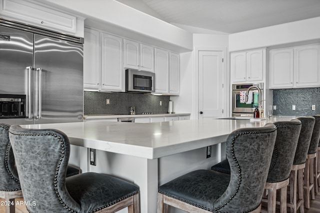 kitchen with a kitchen breakfast bar, decorative backsplash, white cabinetry, and stainless steel appliances