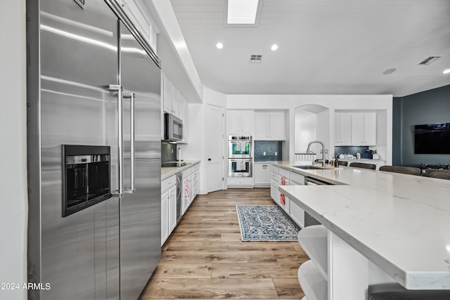 kitchen with white cabinetry, sink, stainless steel appliances, decorative backsplash, and light wood-type flooring