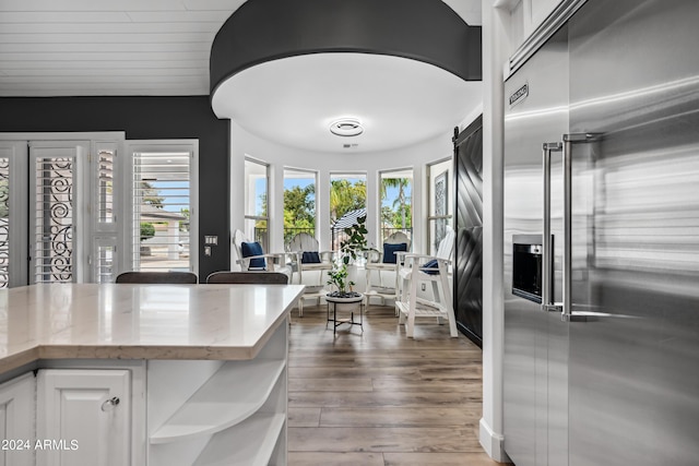 kitchen featuring built in refrigerator, white cabinets, light stone counters, and hardwood / wood-style flooring