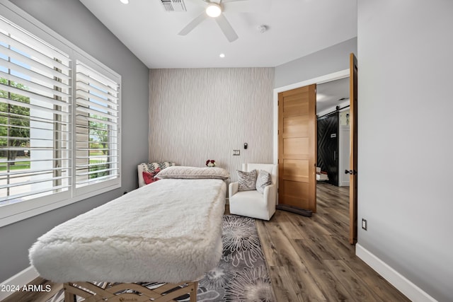 bedroom featuring a barn door, dark hardwood / wood-style floors, and ceiling fan