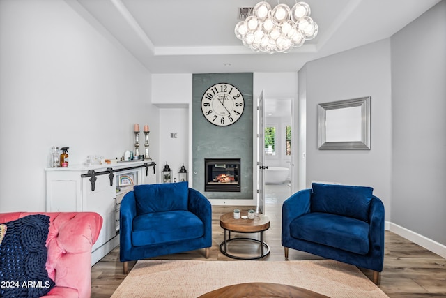 living room featuring a fireplace, hardwood / wood-style floors, a raised ceiling, and a notable chandelier