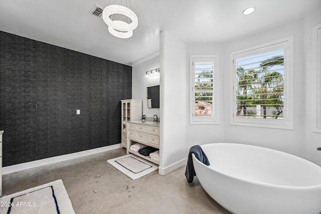 bathroom featuring a notable chandelier, vanity, concrete flooring, and a bath