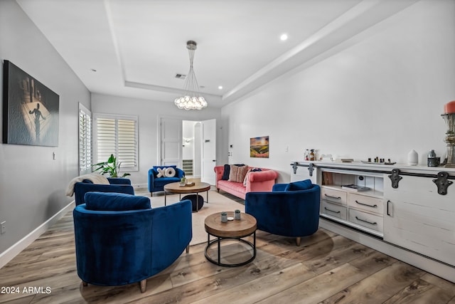 living room featuring a tray ceiling, a notable chandelier, and light wood-type flooring