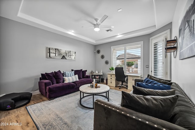 living room featuring ceiling fan, wood-type flooring, and a tray ceiling