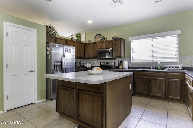 kitchen with a center island, backsplash, light tile patterned floors, appliances with stainless steel finishes, and dark brown cabinets