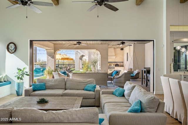 living room featuring ceiling fan, wood-type flooring, beamed ceiling, and a high ceiling