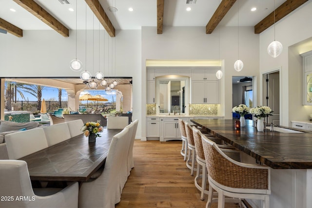 dining room with a towering ceiling, beam ceiling, a notable chandelier, and light wood-type flooring