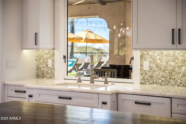 kitchen featuring white cabinetry, light stone countertops, sink, and backsplash