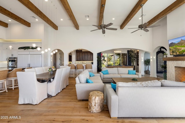 living room featuring beamed ceiling, a towering ceiling, and light hardwood / wood-style floors