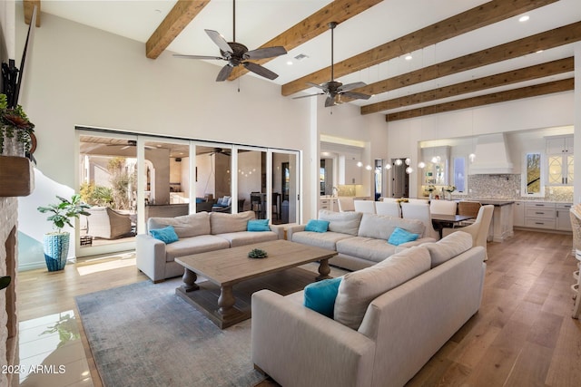 living room featuring a towering ceiling, beam ceiling, light hardwood / wood-style floors, and a wealth of natural light