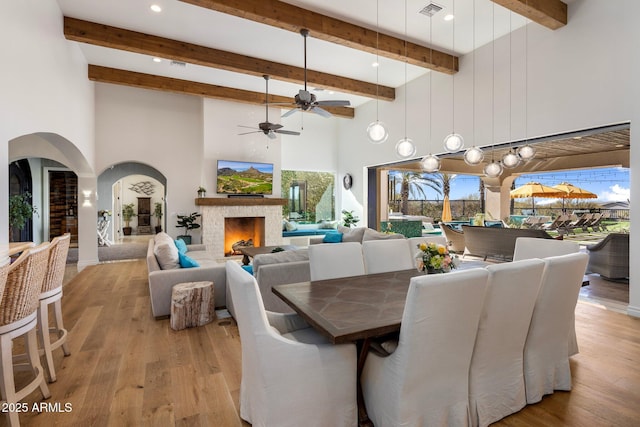 dining space featuring beam ceiling, ceiling fan, a towering ceiling, and light wood-type flooring