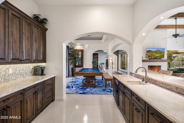 kitchen with dark brown cabinetry, sink, light stone counters, ceiling fan, and decorative backsplash