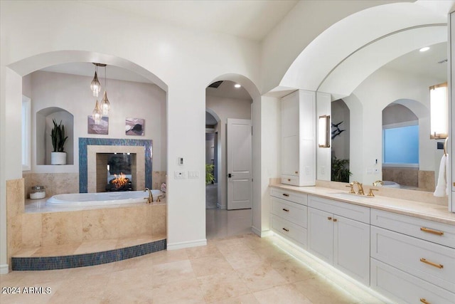 bathroom featuring a tile fireplace, vanity, and tiled bath