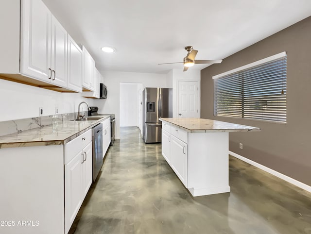 kitchen with stainless steel appliances, white cabinets, a kitchen island, a sink, and baseboards