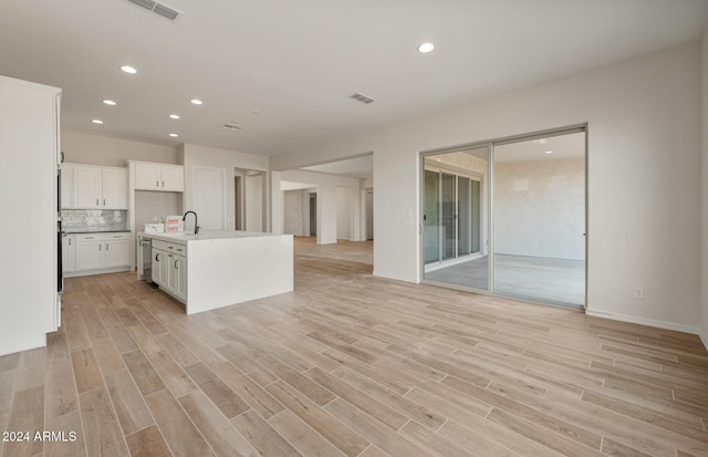 kitchen with white cabinetry, sink, an island with sink, decorative backsplash, and light wood-type flooring