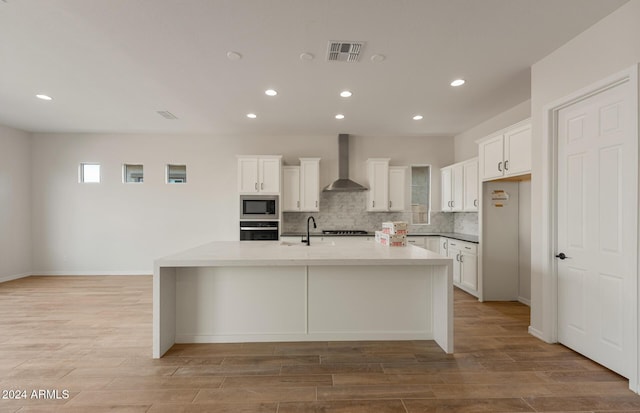 kitchen featuring white cabinets, built in microwave, wall chimney exhaust hood, and stainless steel oven