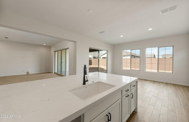 kitchen featuring light stone countertops, light hardwood / wood-style flooring, white cabinetry, and sink