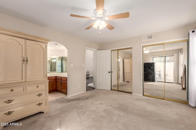 unfurnished bedroom featuring visible vents, connected bathroom, multiple closets, light carpet, and arched walkways